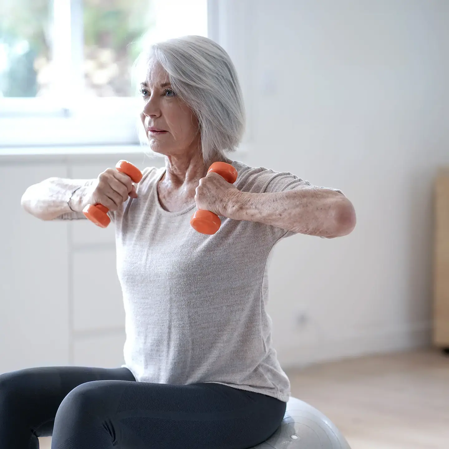 An older woman uses light dumbbell weights to maintain her muscular health.