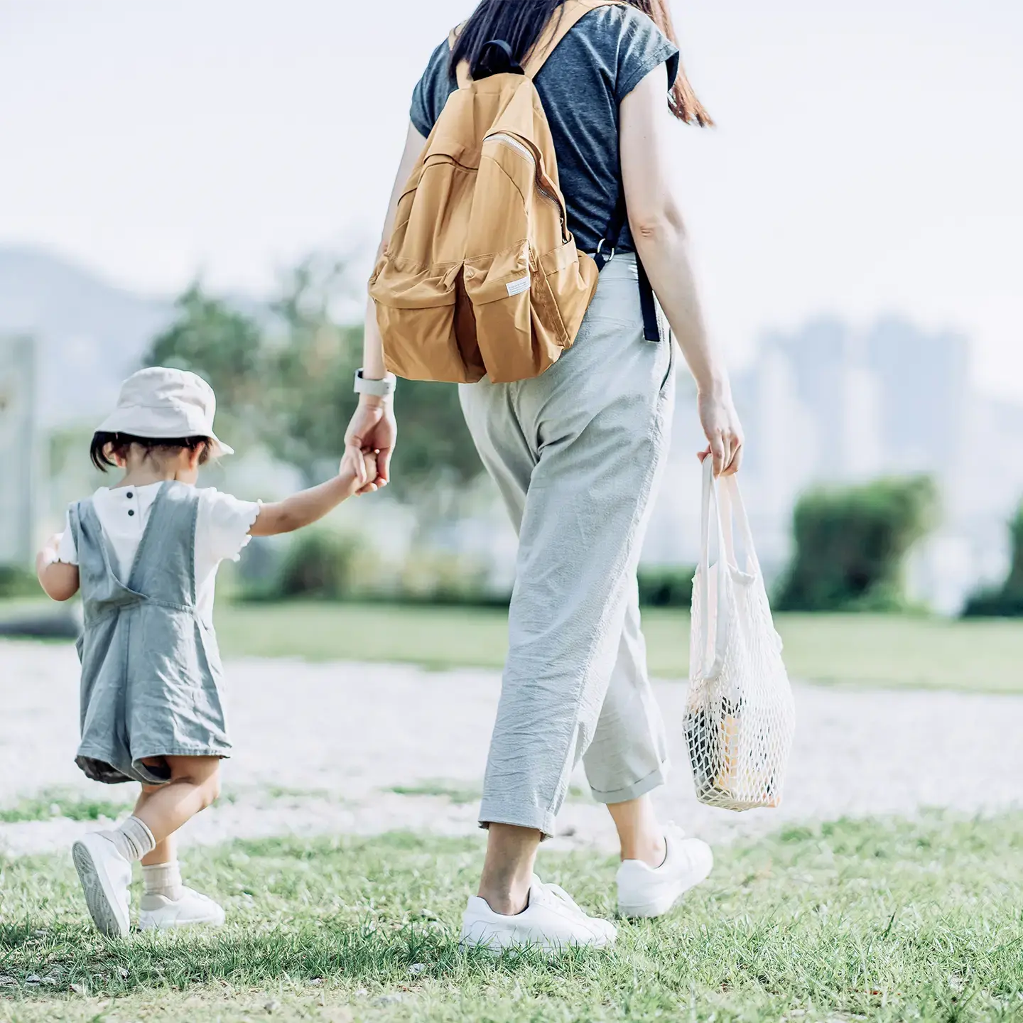 A mother holds her young daughter by the hand as they go for a walk.