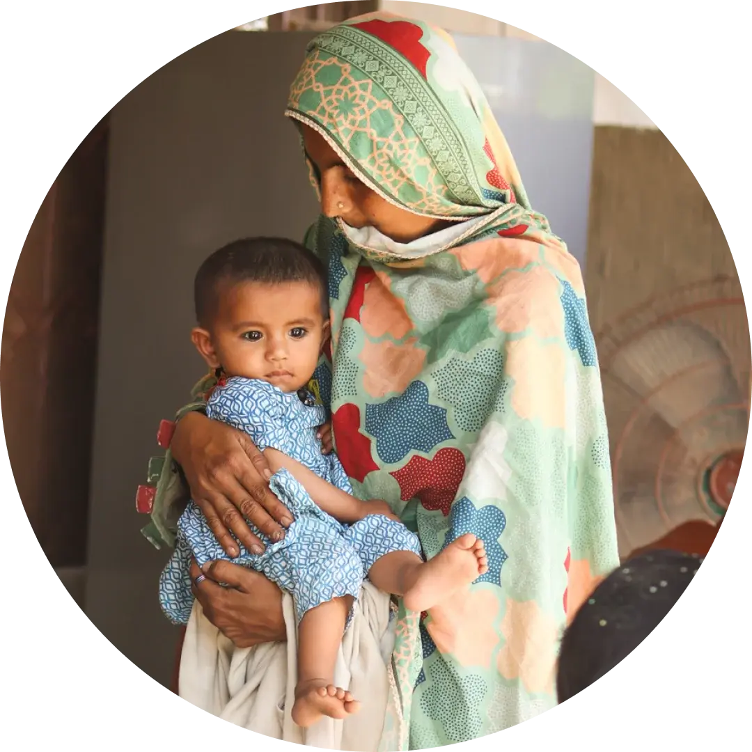 South Asian woman in a patterned headscarf cradling a young child.